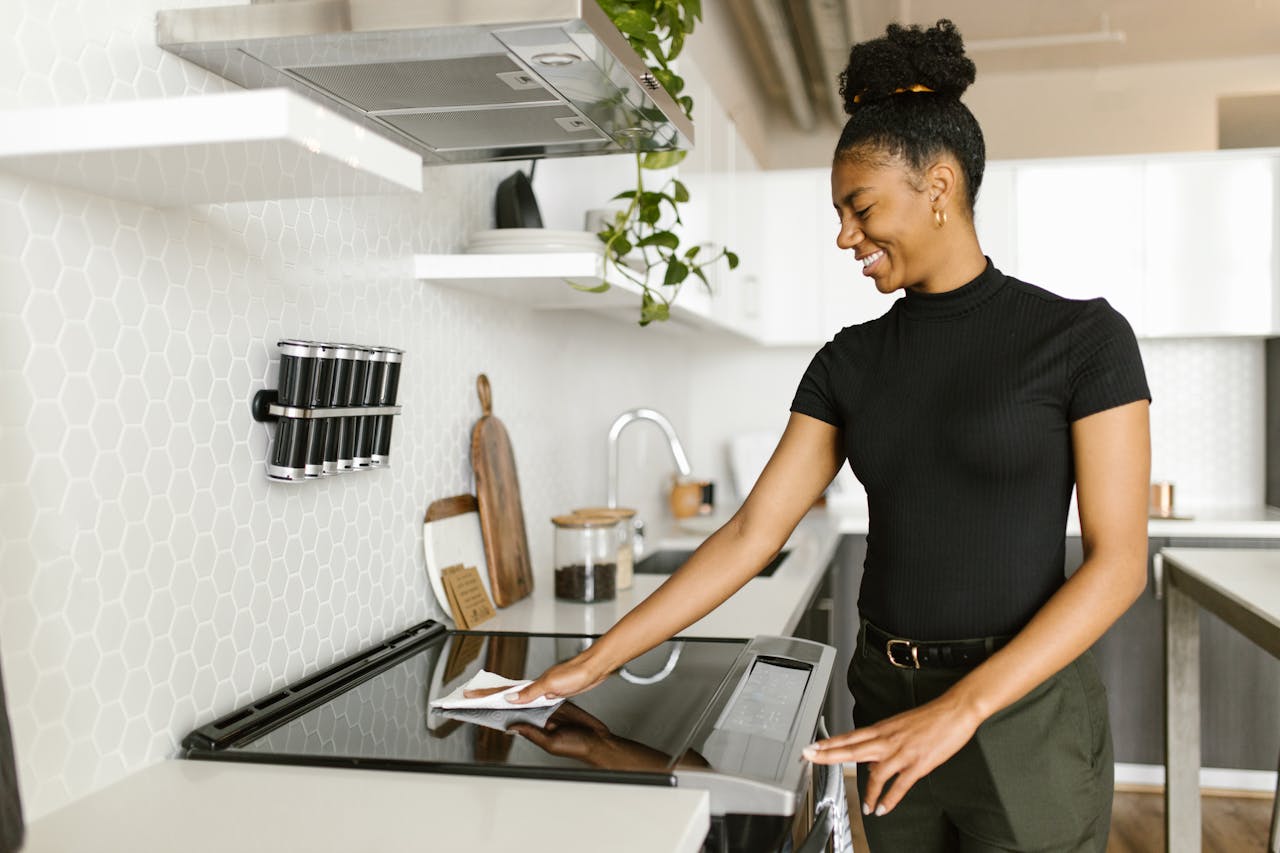 gallery-03 A woman is cleaning the kitchen stove top, showcasing modern housekeeping and responsibility.