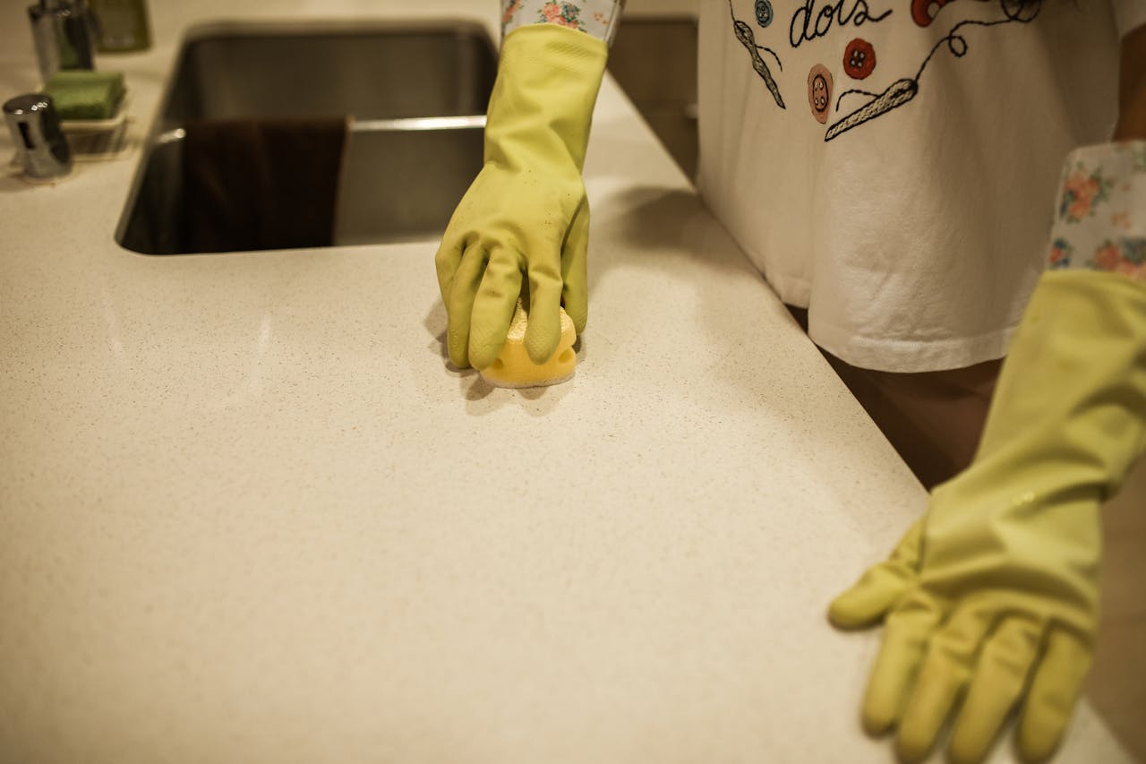 gallery-04 Woman using yellow rubber gloves to clean a kitchen counter with a sponge.