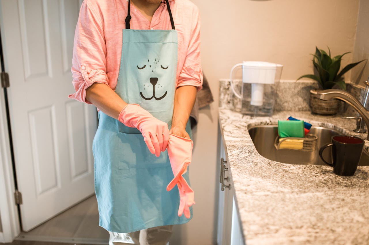 services-img Person in a kitchen putting on rubber gloves with a cute animal-themed apron. Indoor setting.